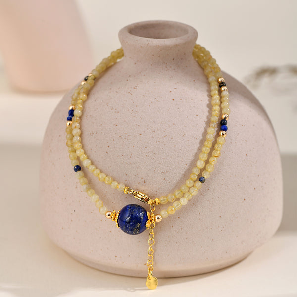 A high-end multi-layer crystal choker necklace featuring delicate golden rutilated quartz micro-beads and a focal royal blue lapis lazuli gemstone, elegantly draped over a minimalist white ceramic vase.
