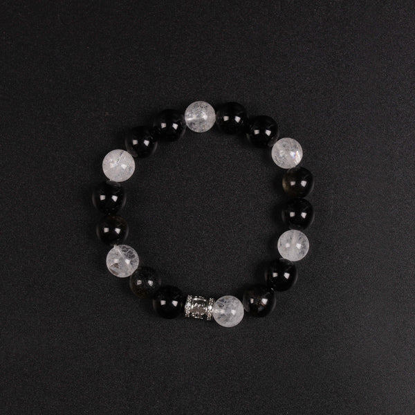 Top-down flat lay view of the circular single-loop dark protection bracelet against a matte black background, showcasing the alternating contrast between deep black obsidian, shimmering gold-sheen elements, and translucent white phantom quartz.