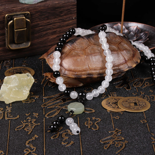 The black and white yin-yang meditation beads draped over a traditional turtle shell artifact, highlighting the high-density volcanic glass texture and a pale green jadeite accent charm.