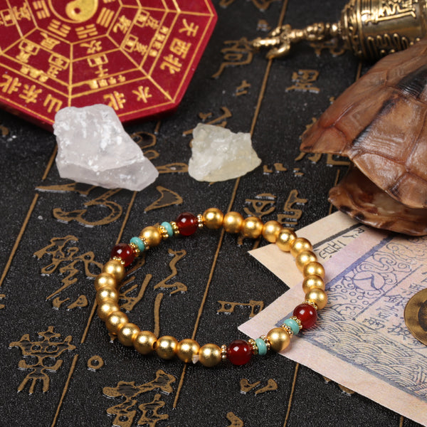 Top-down view of the golden sand bead protection bracelet arranged near a red Bagua clock, a traditional bronze bell, and raw quartz crystals on a dark ritual backdrop.